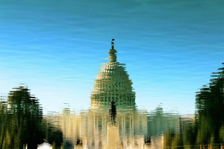 Artistic reflection of the US Capitol on a clear, sunny day over rippling water.